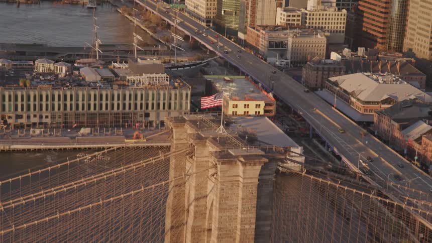 An american flag waving on top of a bridge with buildings roads vehicles and a river in the background