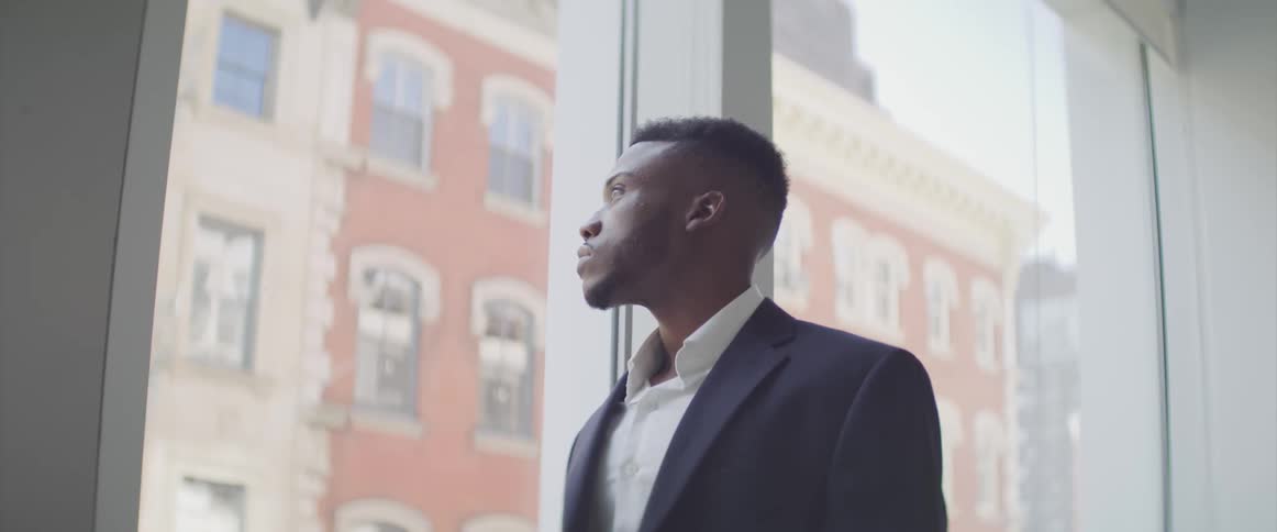 A black man stands at a window and gazes outside
