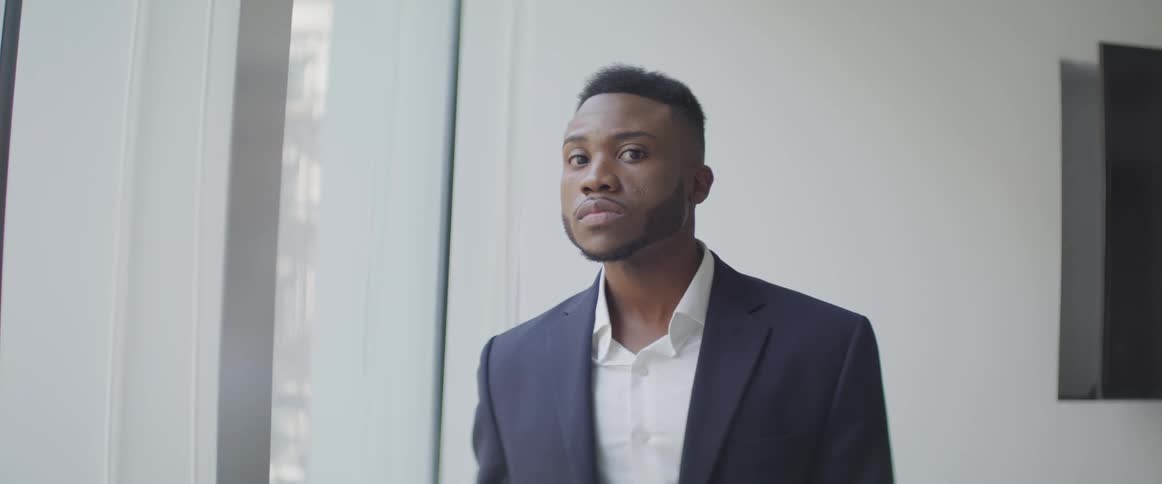 Black businessman looks out the window and turns his head to the camera in the office