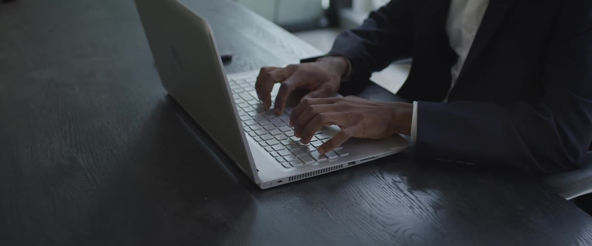 A man sits at a table typing on a laptop
