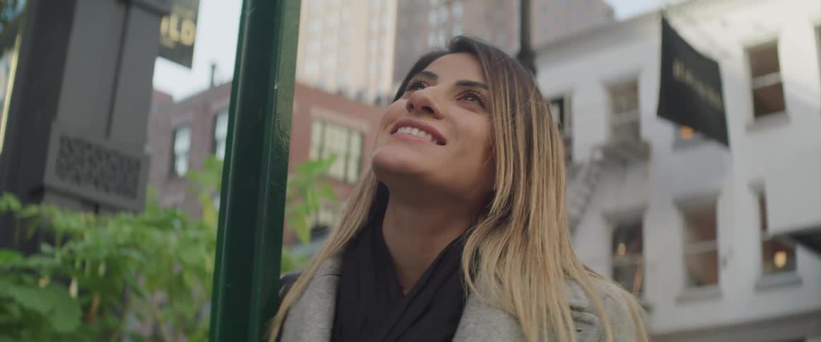 Female leaning on a traffic sign post while looking up in the air smiling as she is watching something in the sky