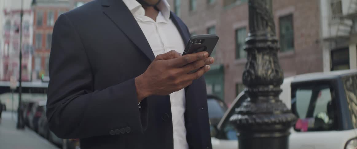A man uses his smart phone while standing on a city sidewalk
