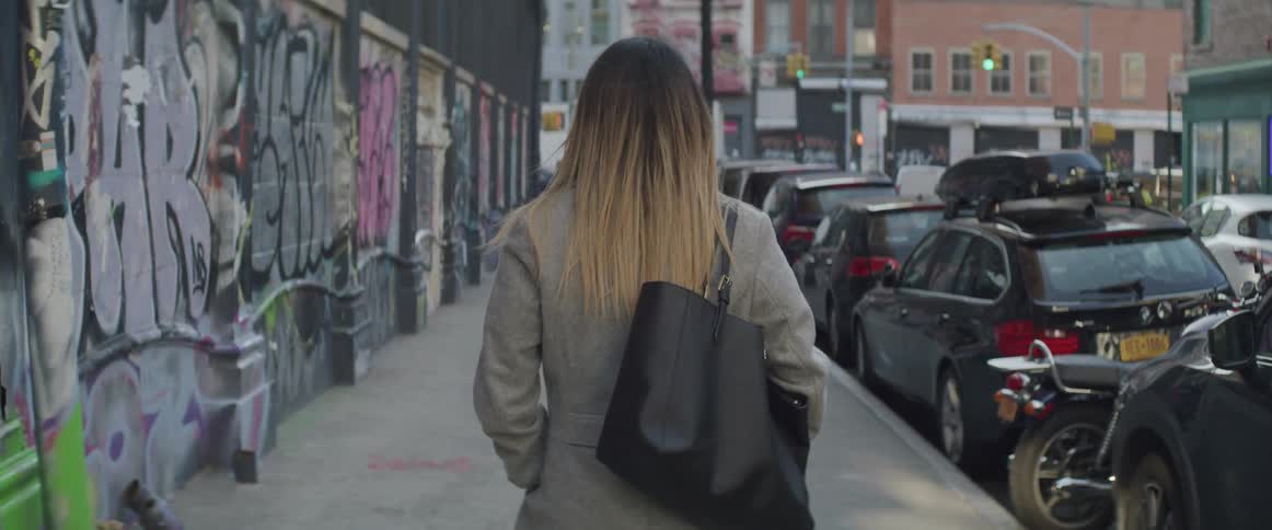 Woman walking on the sidewalk of a city street full of parked cars