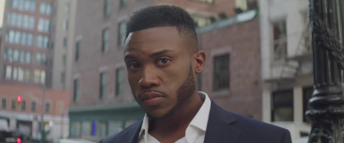 Black businessman looking sideways turns his head to the camera in the street
