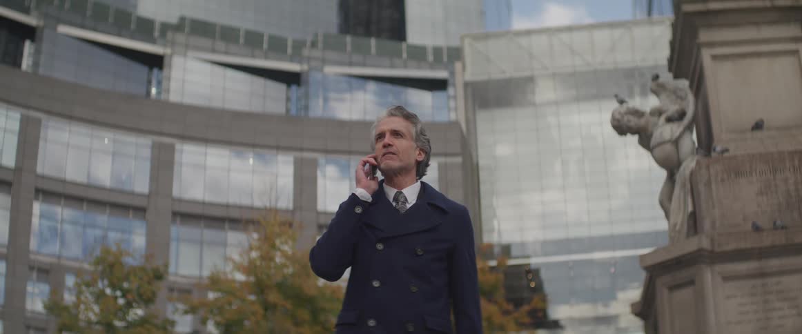 A man stands outside of a building beside a statue and talks on a cell phone