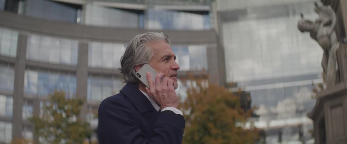 A man stands outside a large building talking on a cell phone