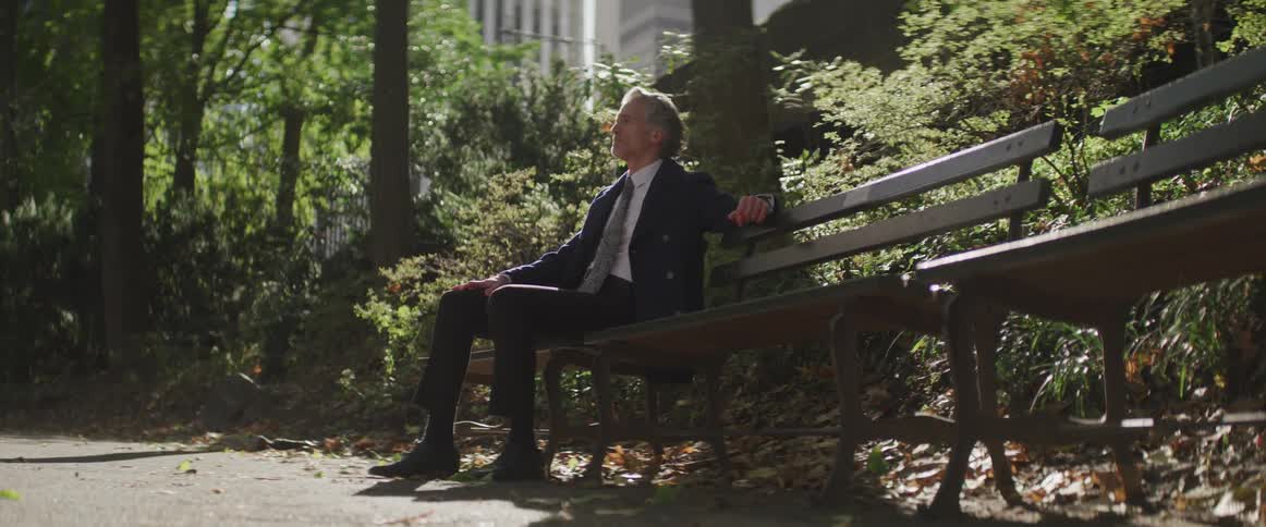 A man sits on a park bench on a sunny day