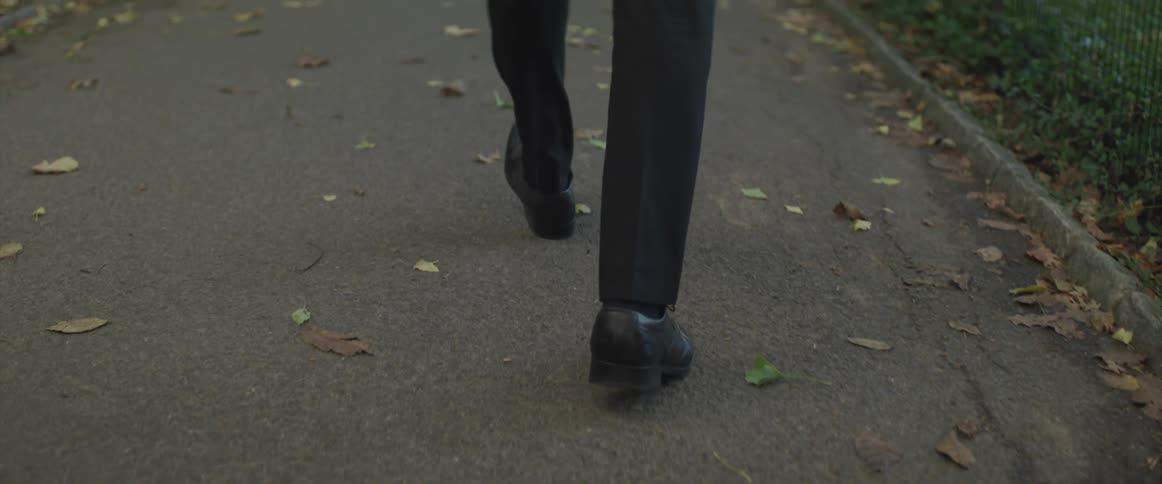 Businessman wearing a suit walks along the pedestrian pathway in the public park