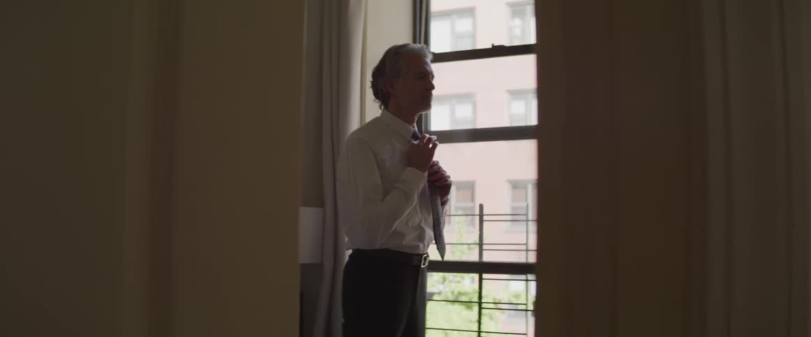 A man standing by a window adjusting his tie