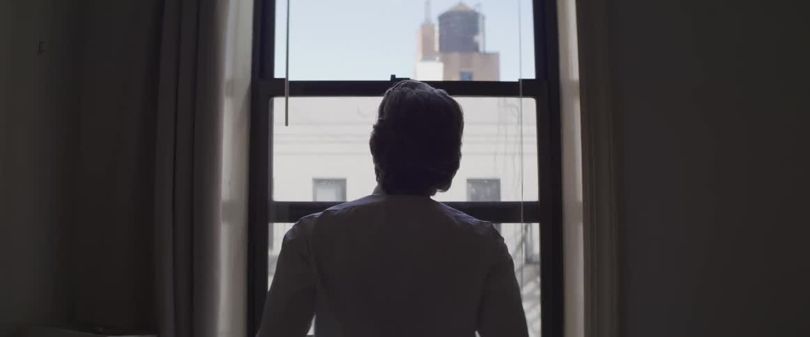 A person stands at a window and looks outside