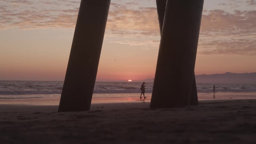 A silhouette of man walks along the beach at sunset next to the ocean