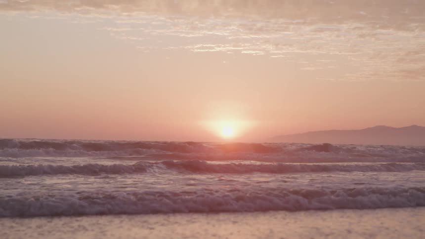 Waves running into a beach under a low sun