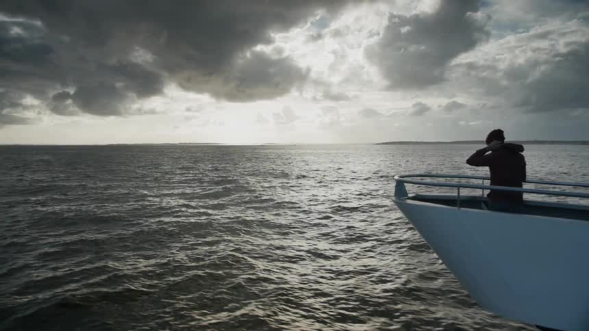 A man stands on the edge of the boat watching the sun rise