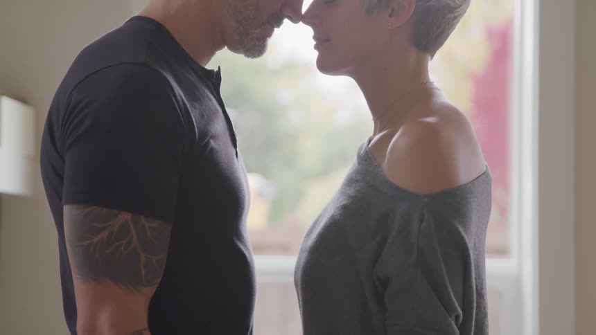 A man and woman stand in their living room and touch their noses to each other