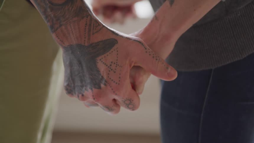Male and female couple stand facing one another and hold hands together
