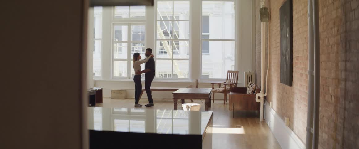Couple embracing one another in front of a large window in an apartment while dancing together