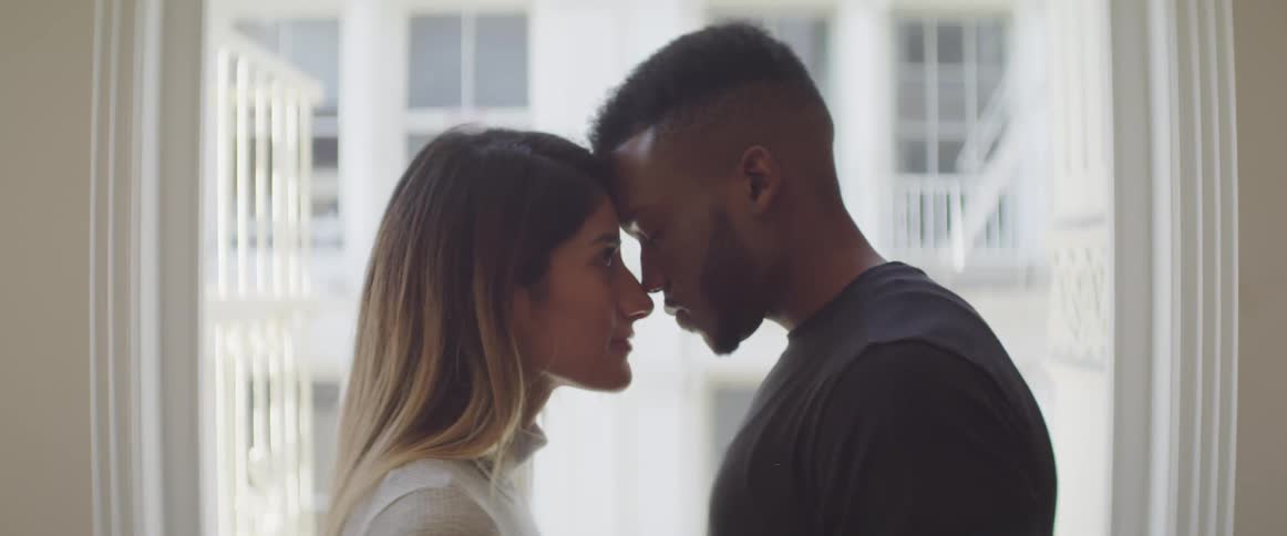 Black man and brunette woman stand face to face in the living room