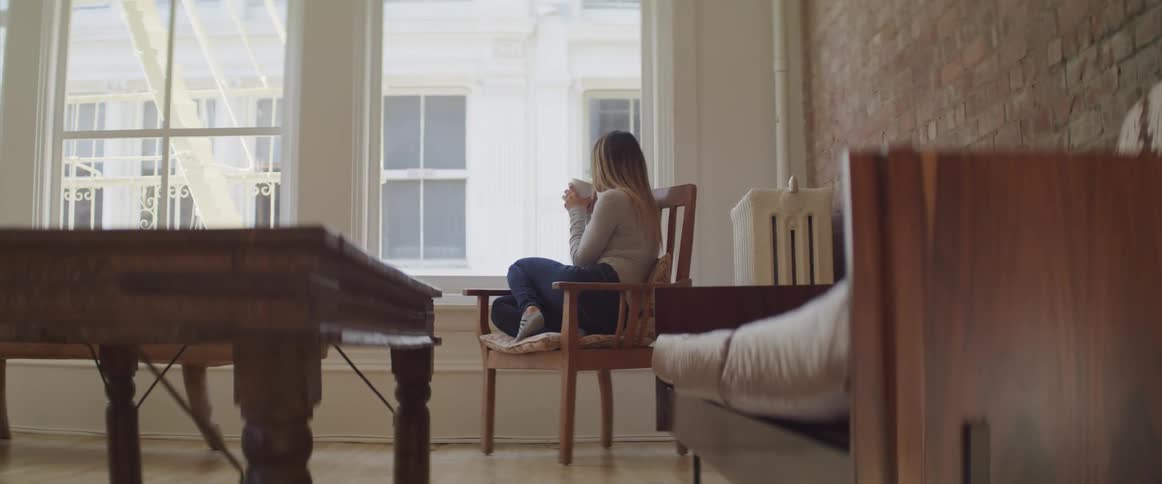 A woman sits on a chair and stares out of a large window