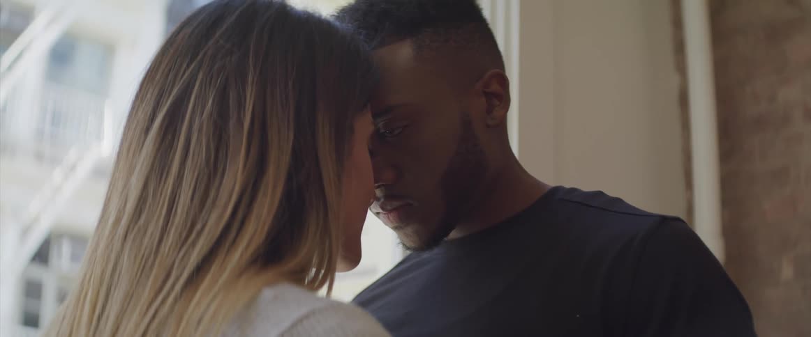Couple stand together leaning heads against each other near window
