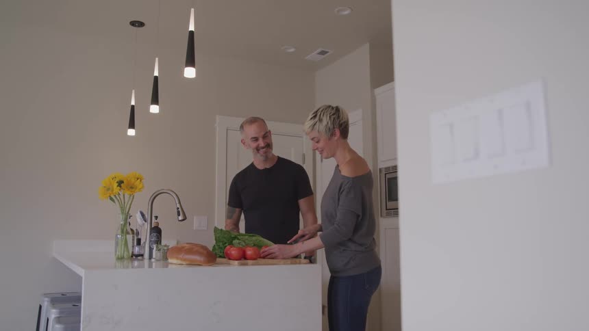 A man and woman are together in the kitchen where she is cutting food