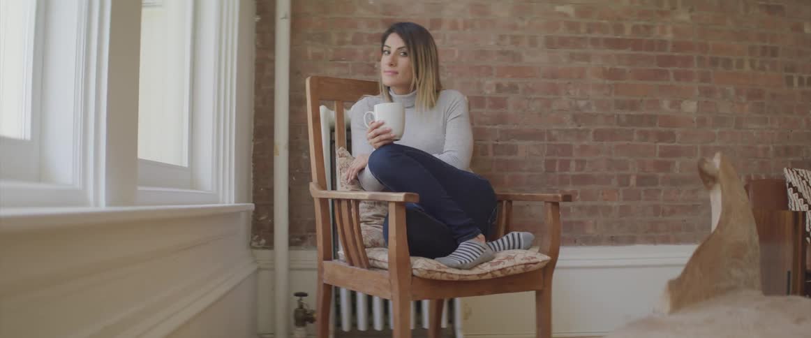 A woman is sitting in the chair drinking from a mug