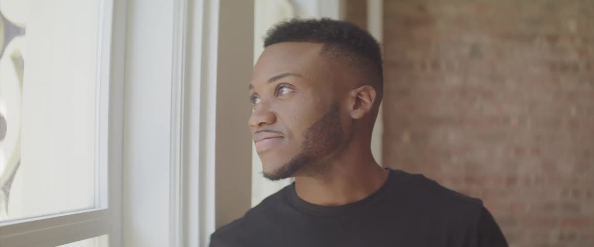 A man looking out of a window while leaning against the window frame