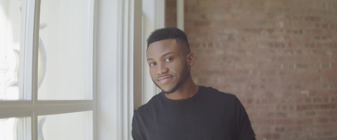 A man leaning against a windowsill while smiling into the camera