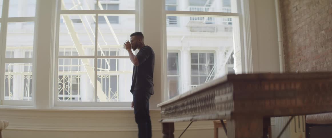 A man takes a drink by a large window