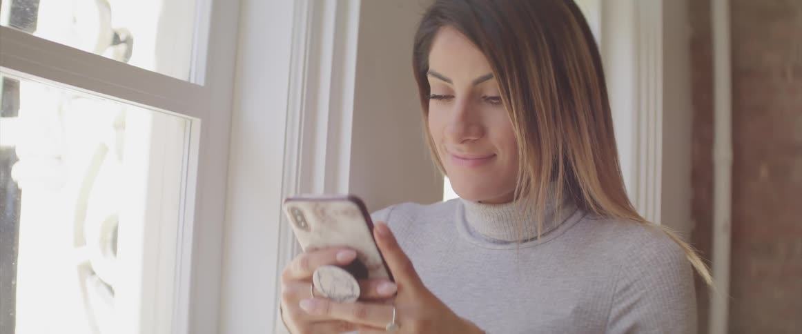 A woman smiles as she looks at her cell phone