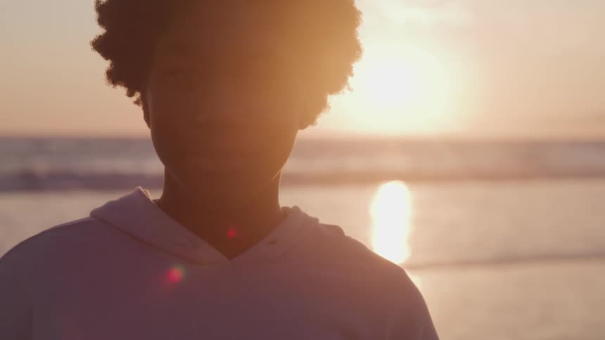 Young black person standing near the shoreline during sunset