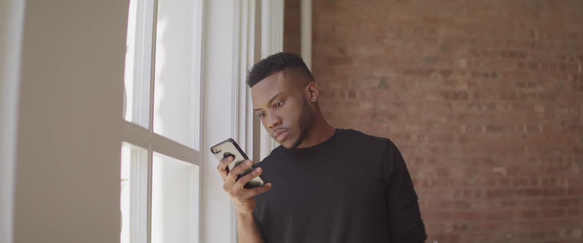 Man standing next to window looks at smartphone