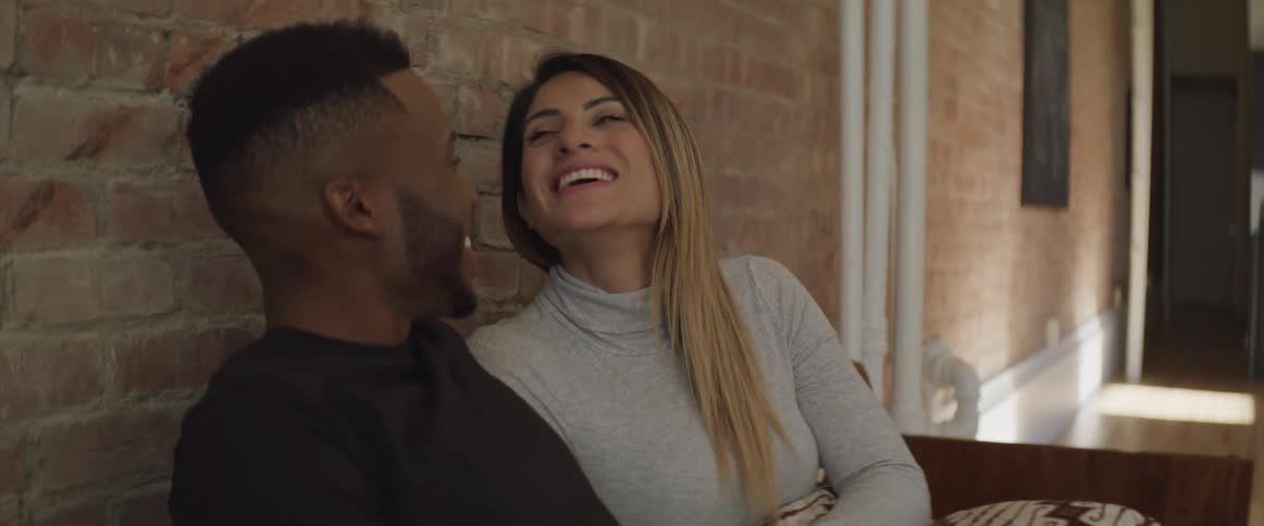 A man and woman sit together on a couch and laugh together