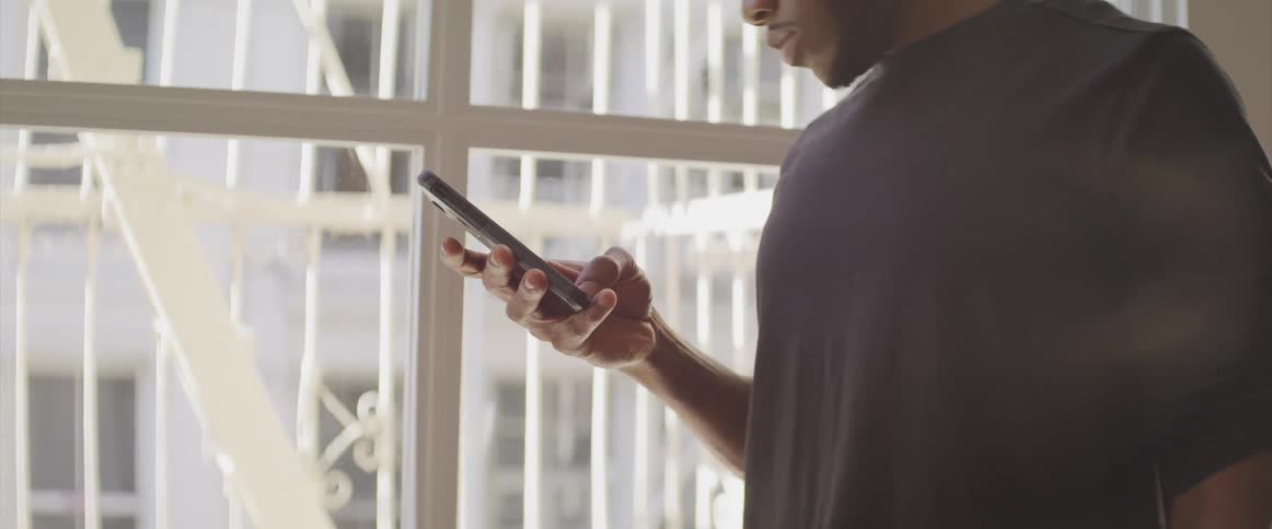Man stands near window surrounded by white scroll work checking his mobile phone