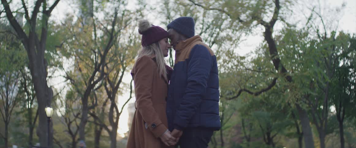 A man and a woman standing face to face holding hands with trees in the background