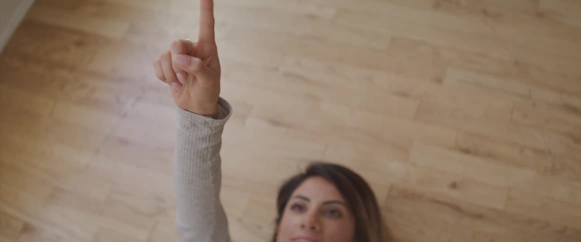 Woman lays on the floor and points towards the ceiling with her index finger