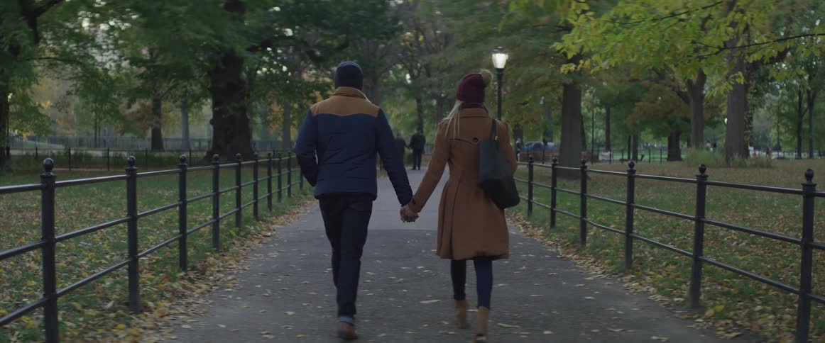 A man and woman hold hands walking a public park pathway