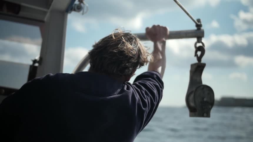 A man leans against the side of a ship to look out over the water