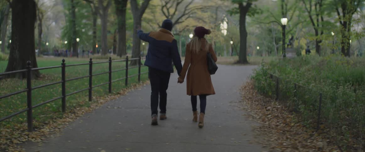 Romantic couple holding hands while walking through the park at dusk