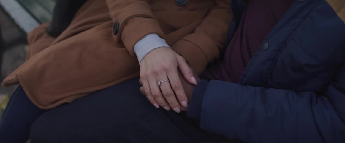 A woman rubbing a mans hand as they sit together on a wooden bench outdoors