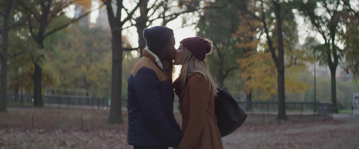 Black man and white woman kiss each other in the public park