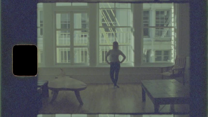 Woman stands in apartment in front of windows looking at camera