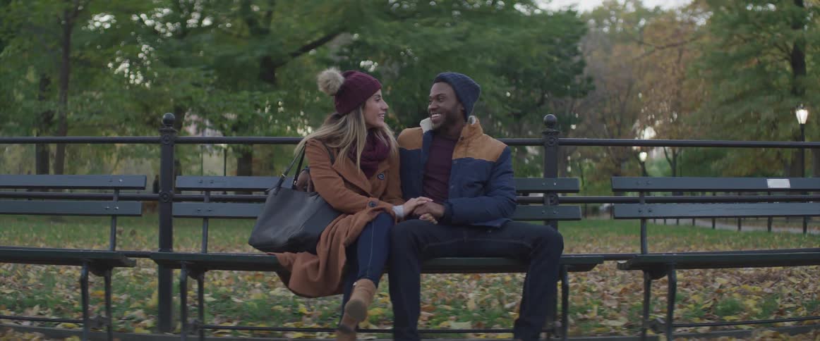 A woman touches her boyfriends hand as they sit on a bench in a park