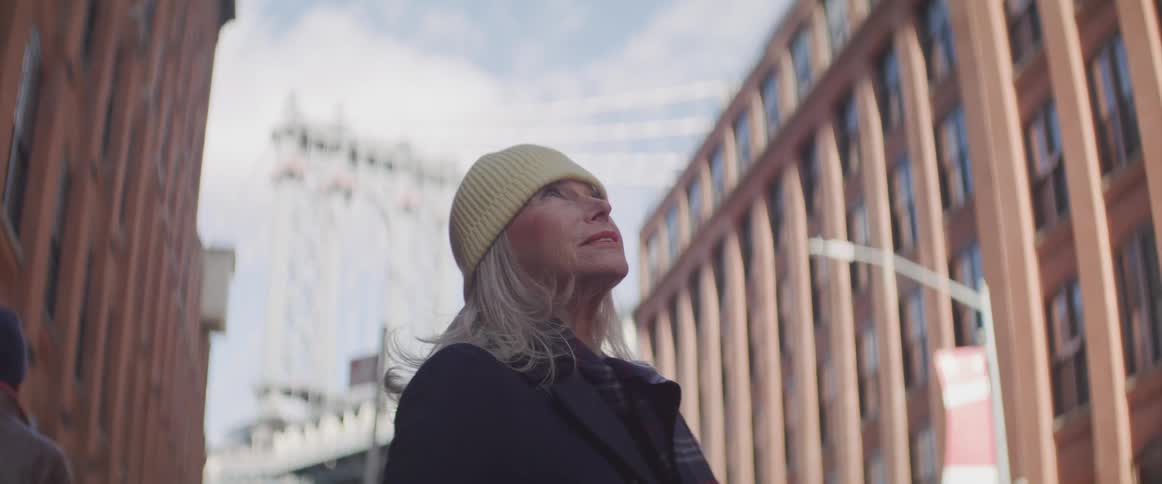 A woman stands in a street and looks up at the buildings