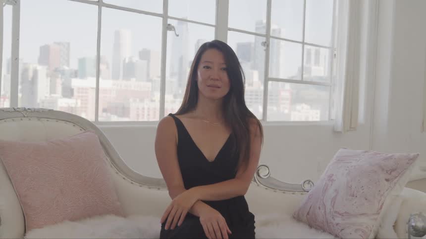 A woman is sitting on a white couch in front of a window