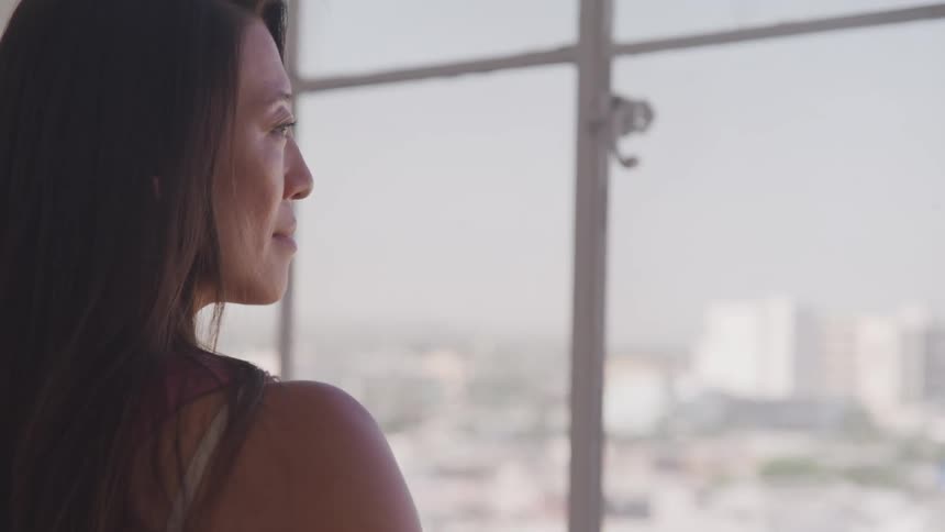 Asian woman looks out the window and smiles slightly