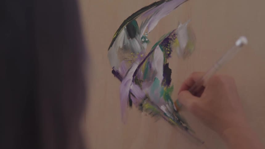 Female applying coloring with a flat paint brush to a painting on a canvas near a window
