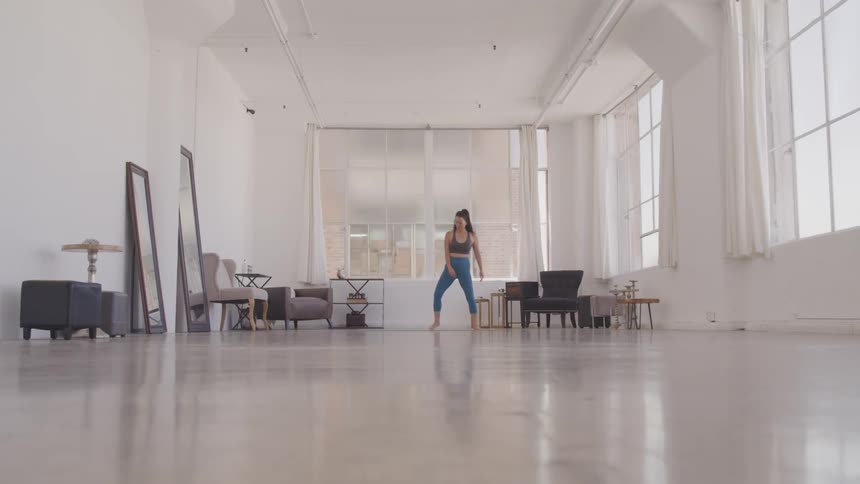 A woman walking in a room then turns around and start stretching