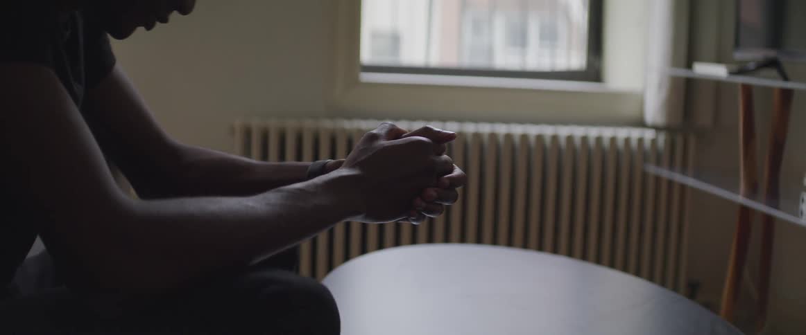 A man sits in his living room with his bed bowed down and his arms on his knees
