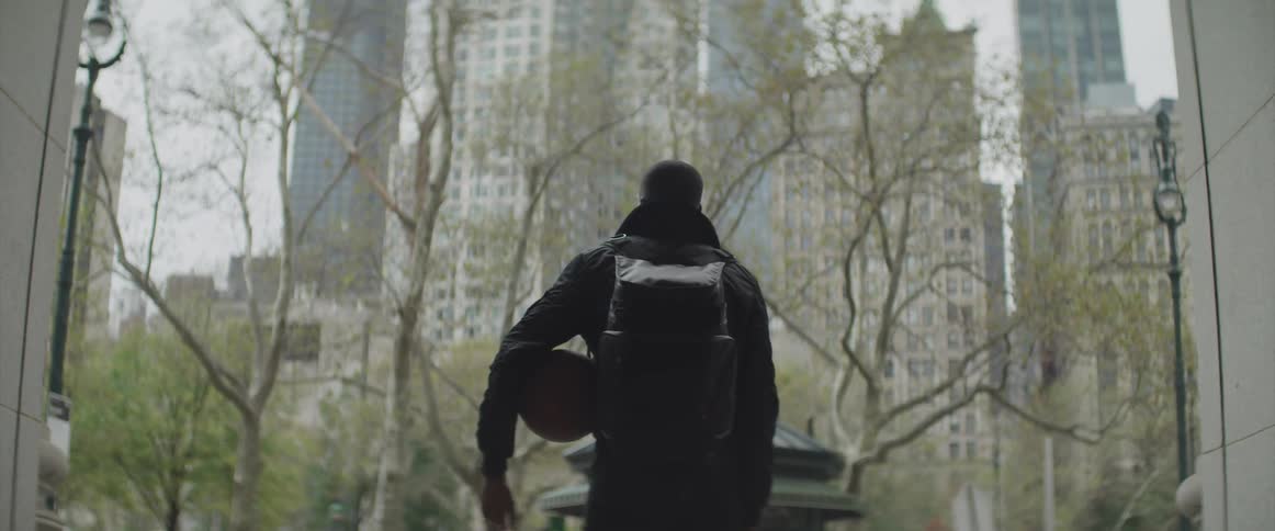 Black man holding a ball stands and looks at the high rise buildings