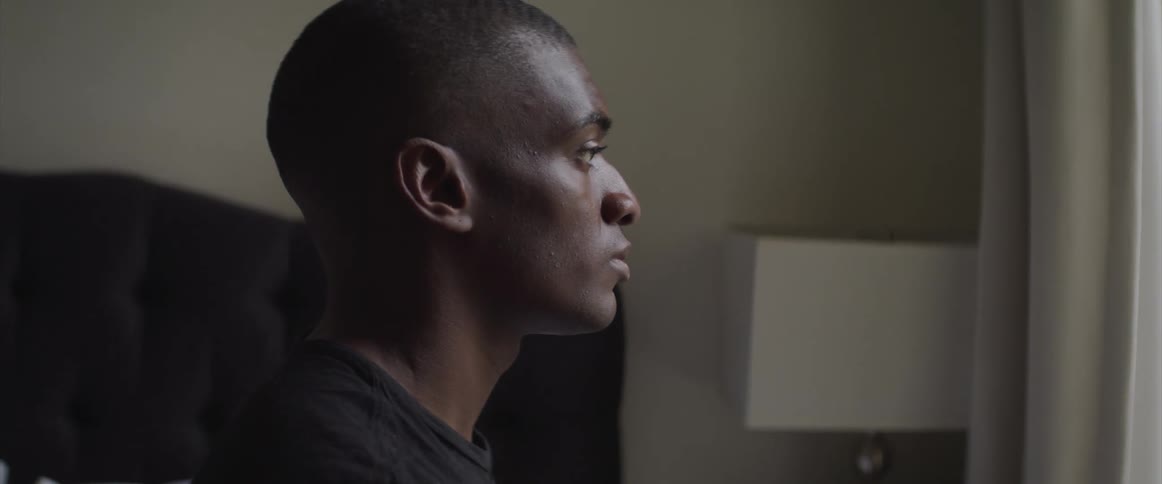 A man is sitting on his bed looking out the window
